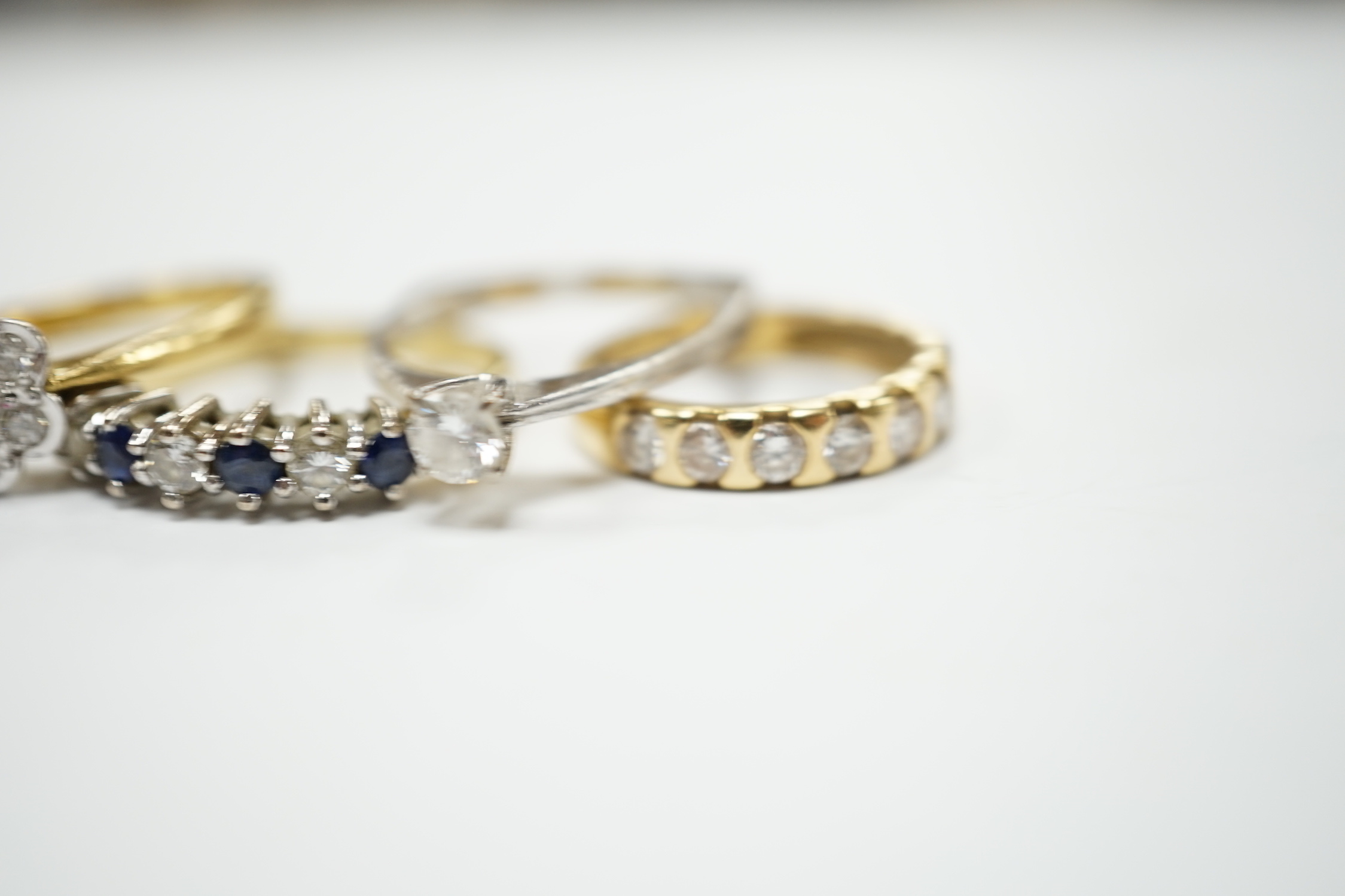 Four assorted 18ct and diamond set rings, including solitaire, flower head cluster, three stone crossover and seven stone half hoop, together with and 18ct sapphire and diamond set half hoop ring, gross weight 15.6 grams